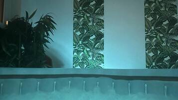 A room with a bed, a wall with a tropical leaf pattern, and a plant on the left.