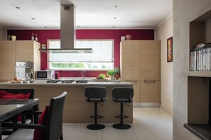 A modern kitchen with a central island, bar stools, and a dining area with a red chair. - Villa in the heart of Tuscany (Rigutino)