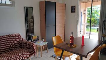 A modern living room with a sofa, a dining table with chairs, a small side table, and a wooden cabinet.