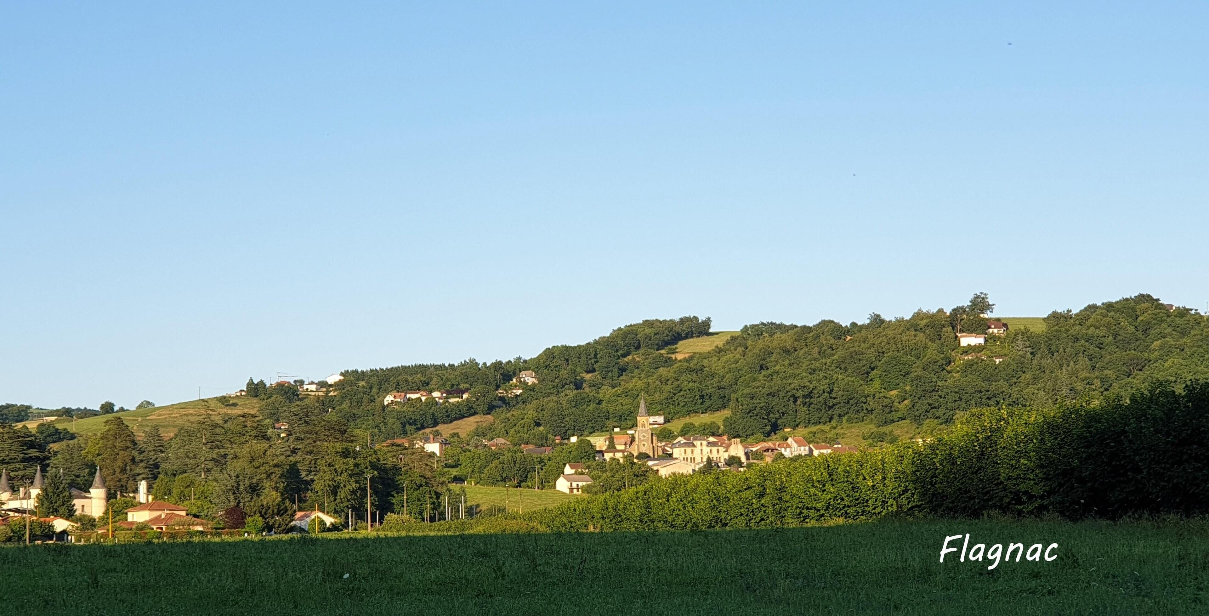 A rural landscape with a village on a hill, including buildings and greenery.