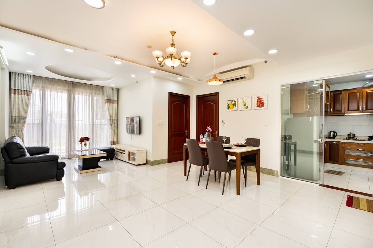 Una sala de estar moderna con comedor, sofá, mesa de centro y cocina con alacenas de madera y puerta de cristal.