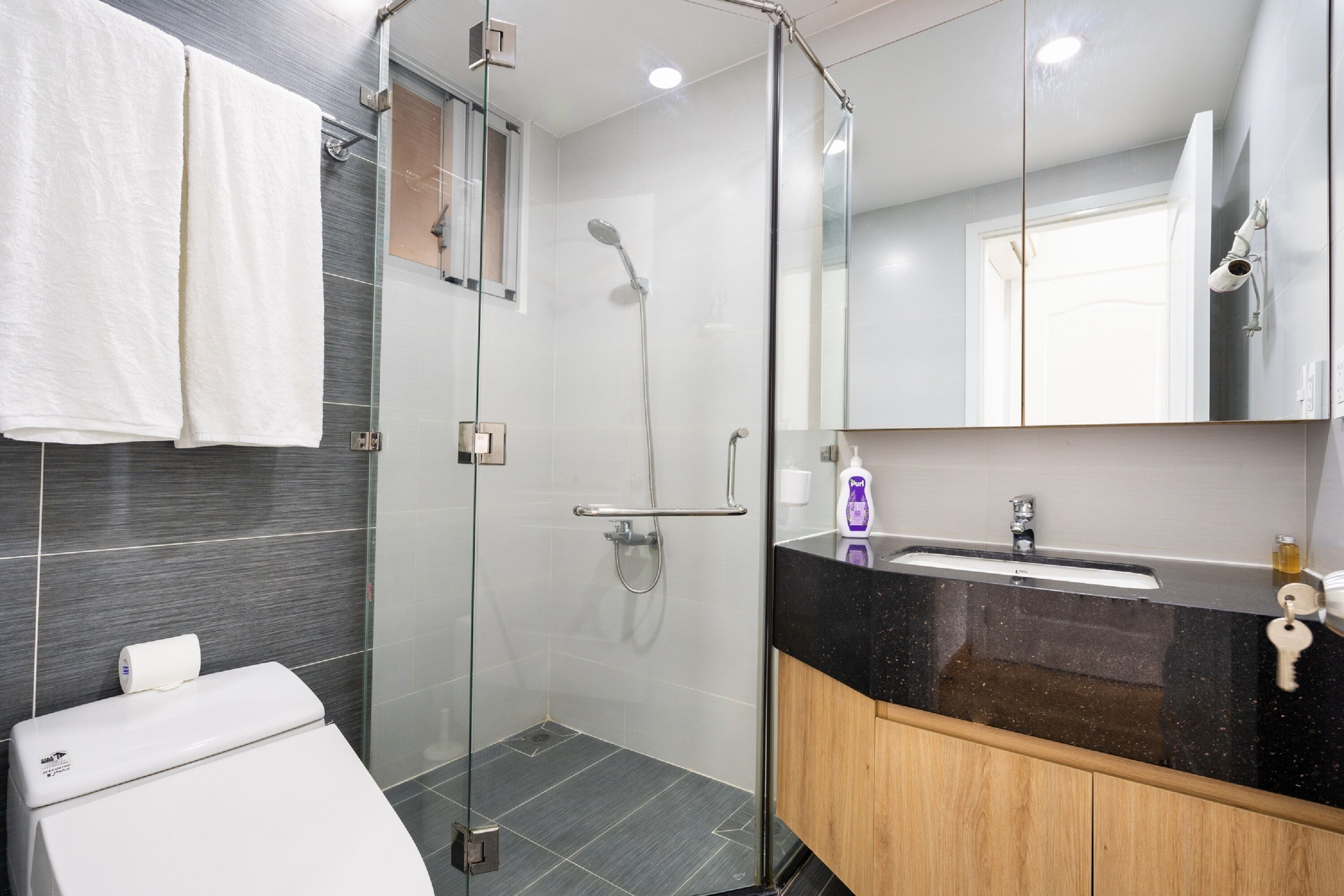 A modern bathroom with a glass-enclosed shower, a white toilet, a black countertop sink, and a wooden cabinet.