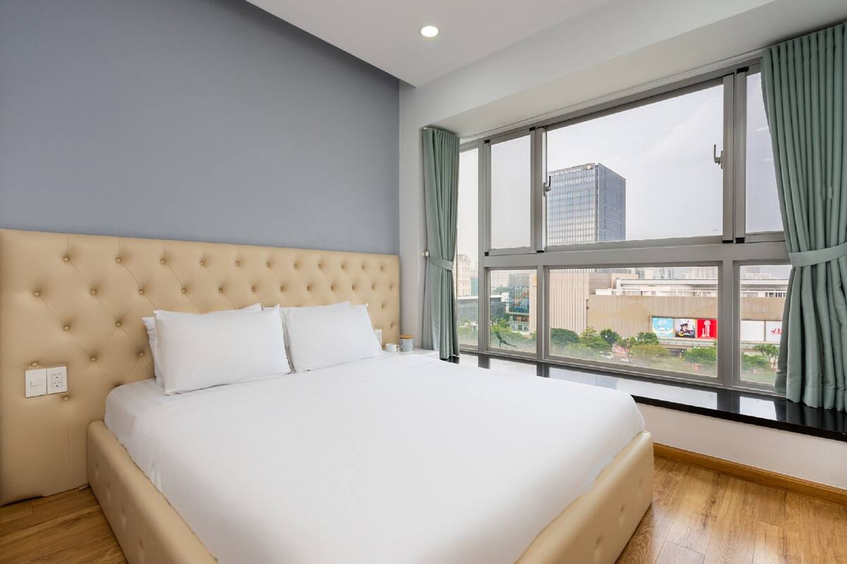 Habitación de hotel con una cama grande, una ventana con cortinas y vistas a edificios.