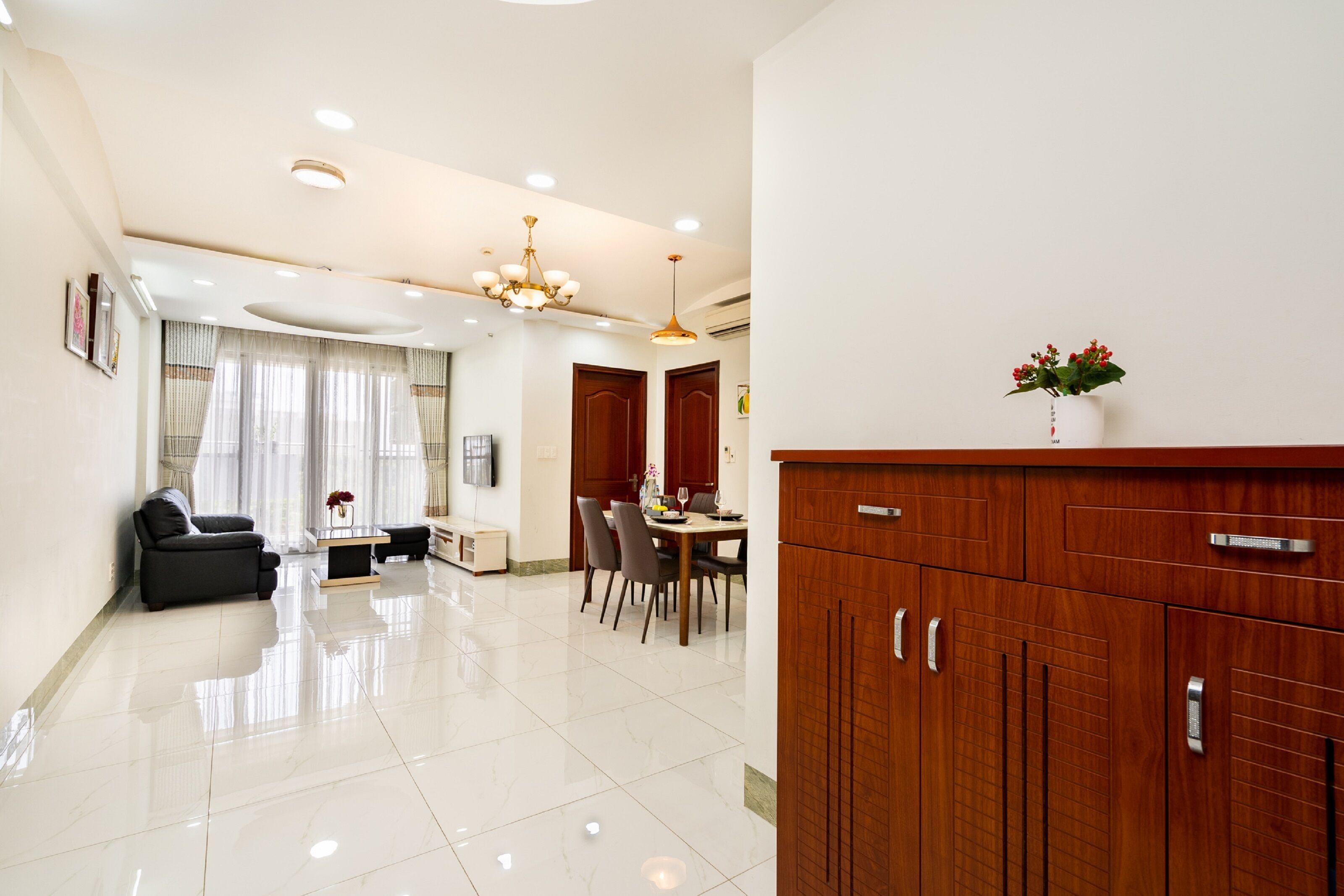 Una sala de estar moderna con sofá, mesa de comedor, sillas, un aparador de madera y una araña.