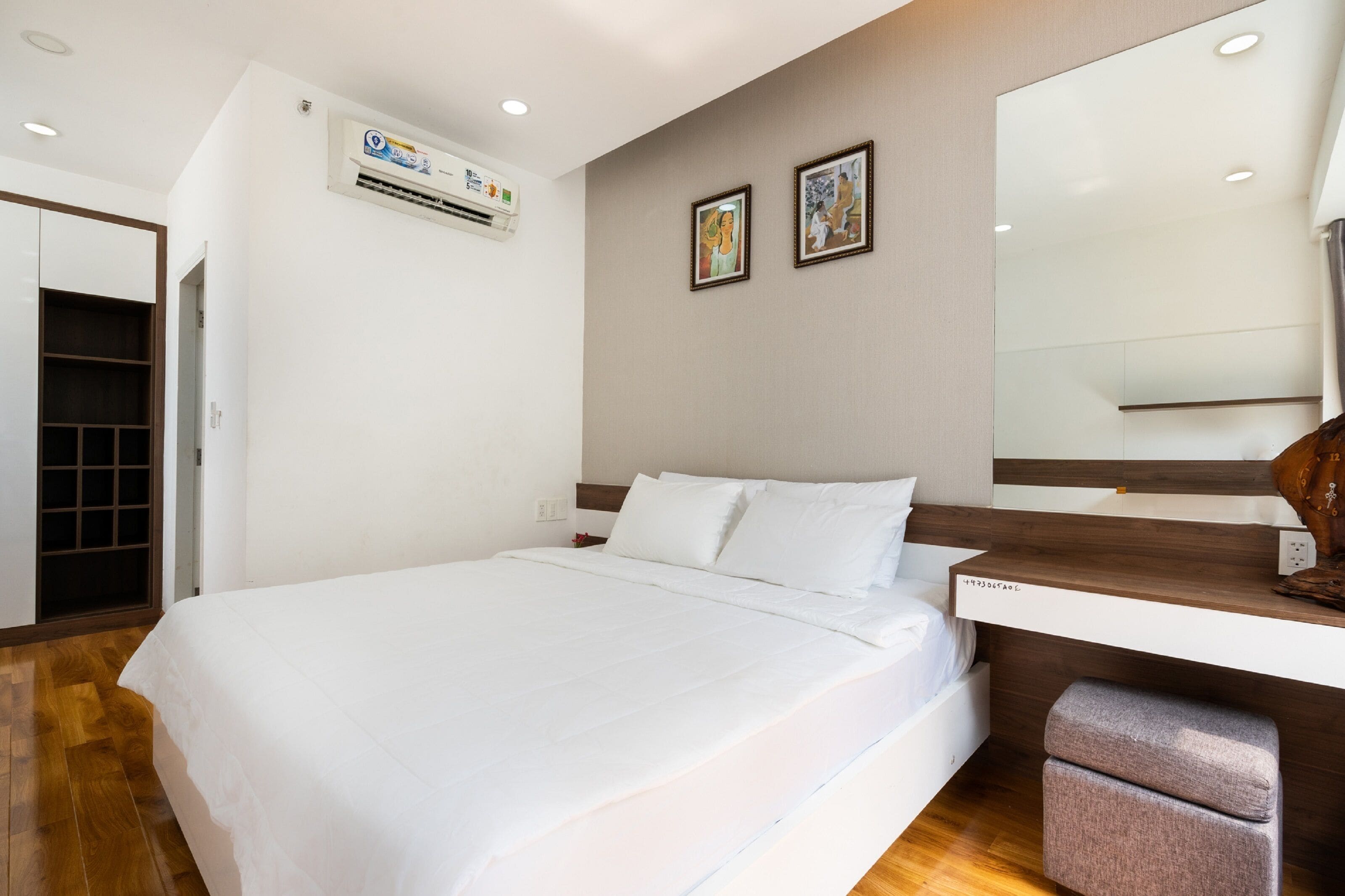 Moderni hotellihuone, jossa on suuri sänky, puinen yöpöytä, peili ja seinälle asennettu ilmastointilaite.