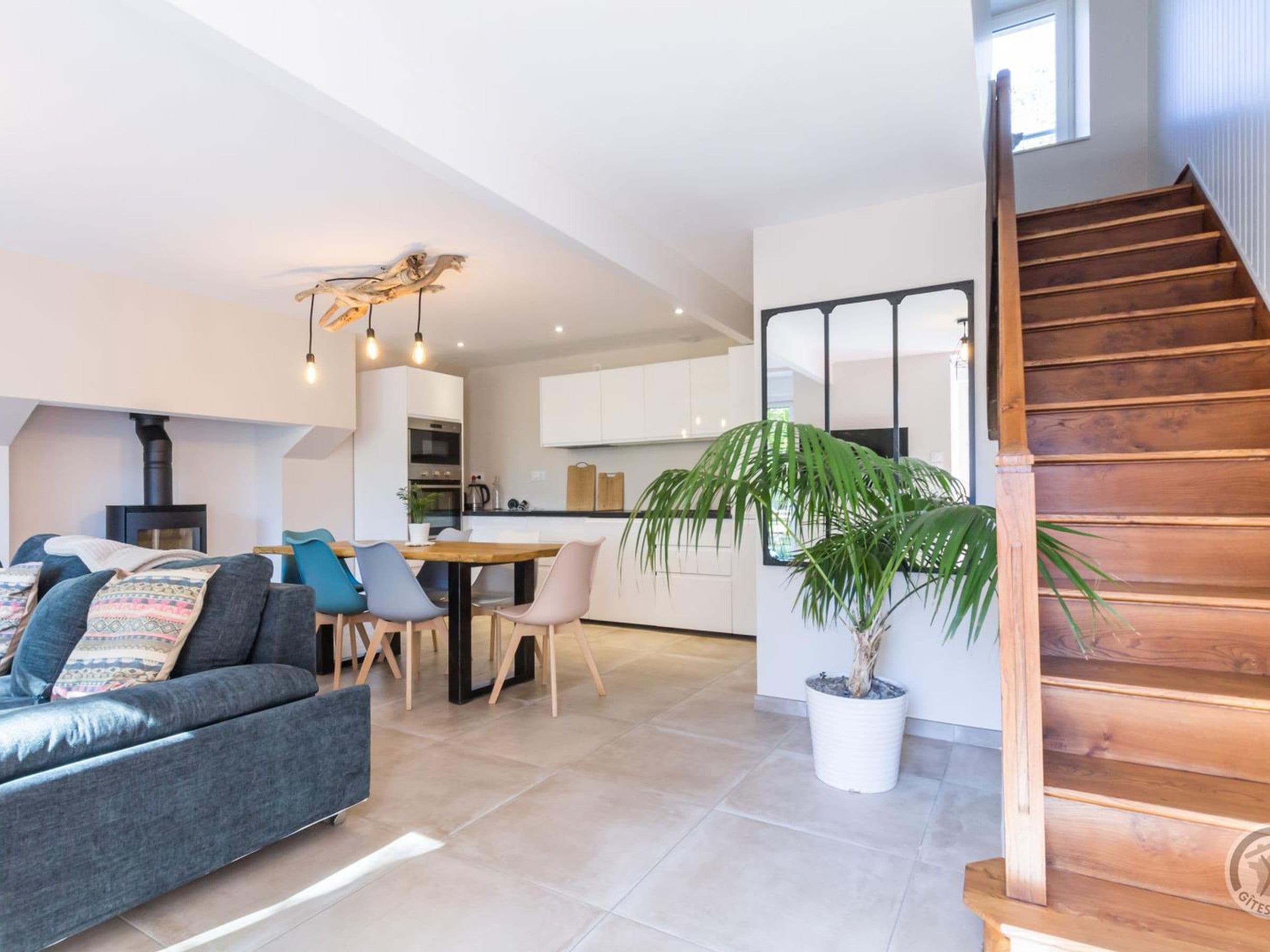 A modern living space with a sofa, dining table, chairs, a potted plant, and a wooden staircase.