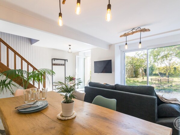 A modern living room with a wooden dining table, a sofa, and a TV mounted on the wall.