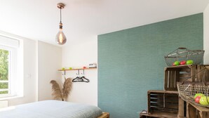 A bedroom with a wooden bed, a hanging light fixture, a wall-mounted shelf with apples, and a rustic wooden structure with baskets.