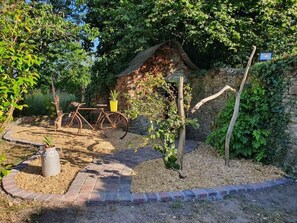 A rustic garden with a vintage bicycle, a small stone structure, and a potted plant.