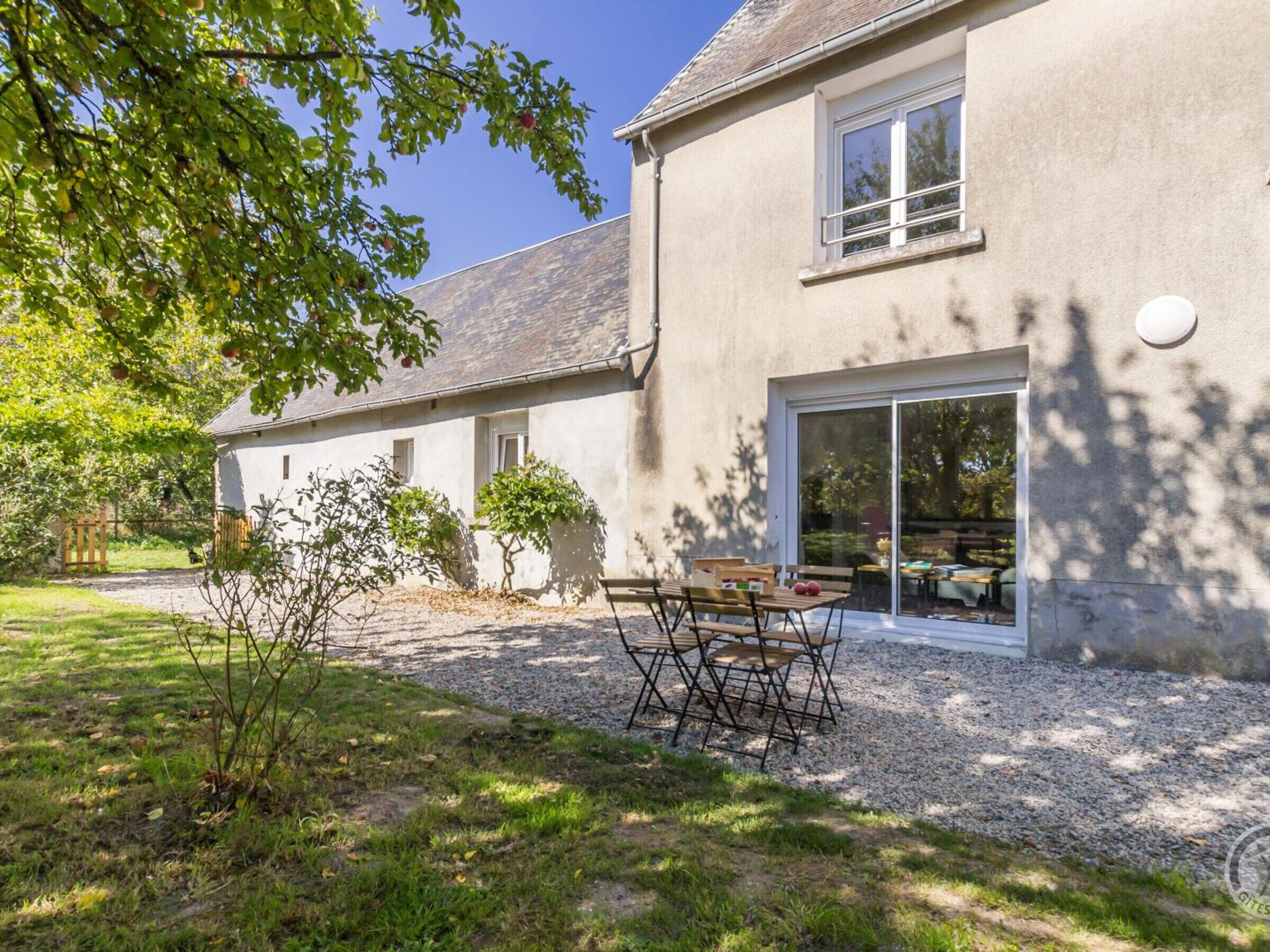 Une maison à deux étages avec une allée en gravier, une terrasse dotée de meubles d’extérieur et une grande porte-fenêtre coulissante donnant sur une salle à manger intérieure.