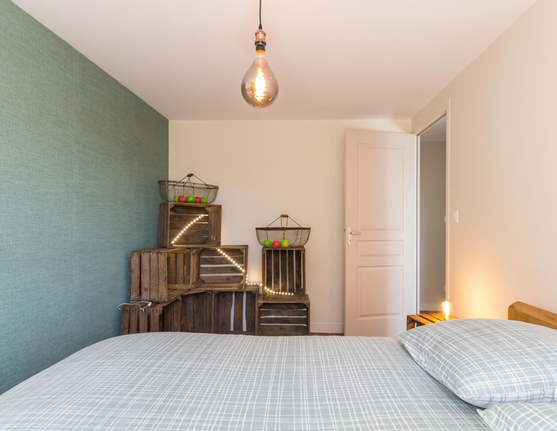 A bedroom with a bed, a hanging light fixture, and decorative baskets on wooden crates.