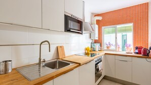 Una cucina moderna con mobili bianchi, un lavello in acciaio inossidabile, un forno a microonde e una finestra con piante in vaso.