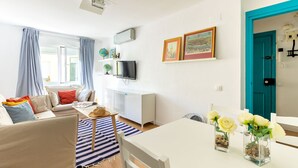 Un soggiorno moderno con divano, tavolo da pranzo e TV a parete. Si notano due quadri appesi, un globo e una piccola libreria con oggetti decorativi.