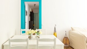 Un tavolo da pranzo bianco con sedie, una porta con cornice blu, un divano bianco e un lampadario.