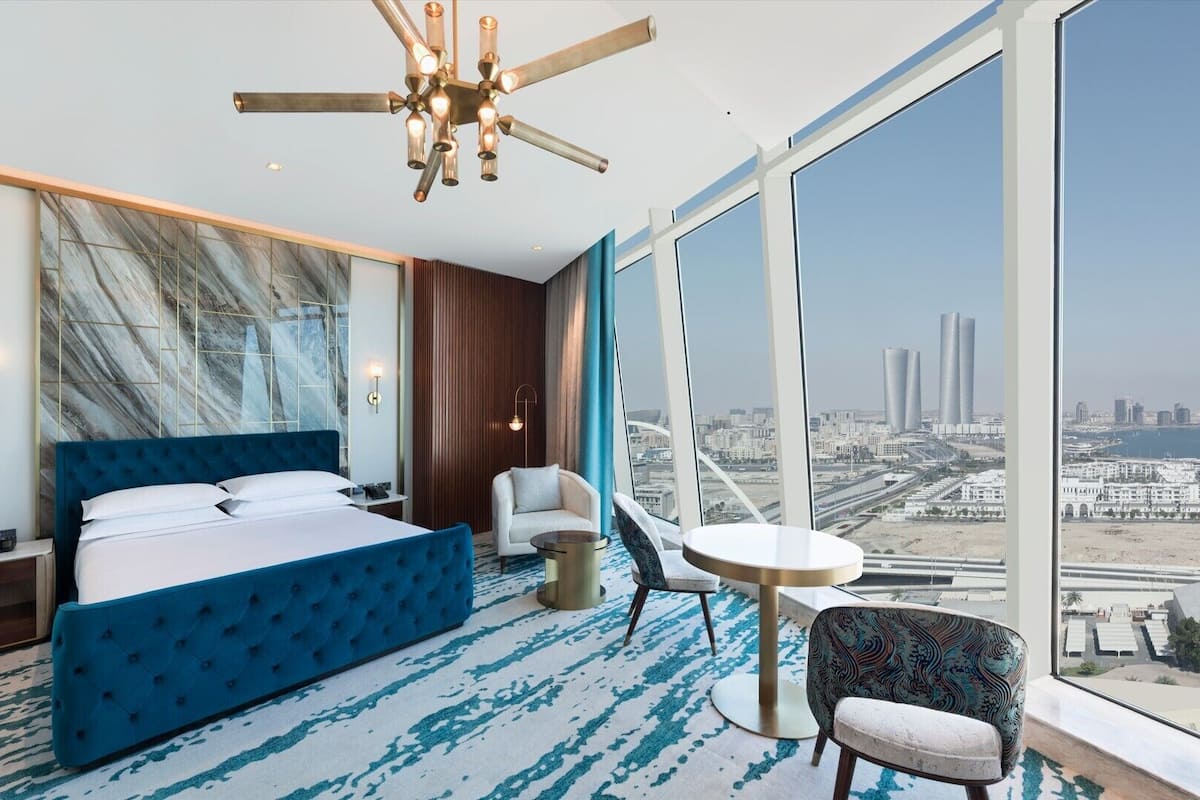 A modern hotel room with a large bed, a seating area, and a city view.
