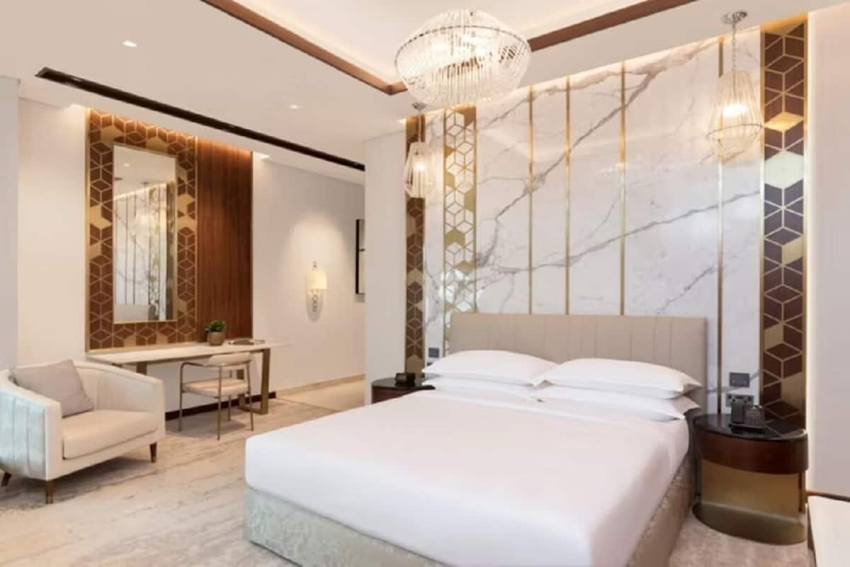 A modern hotel room with a large bed, a desk, a chair, and a mirror.
