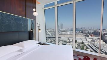 A modern hotel room with a large bed, a marble accent wall, and a city view through floor-to-ceiling windows.