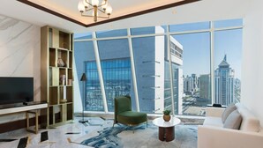 A modern living room with a large window, a flat-screen TV, a green armchair, a white sofa, and a floor lamp. - Velero Hotel Doha Lusail (Doha)
