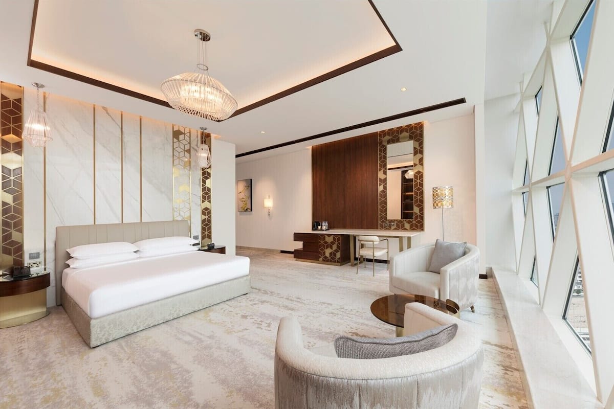 A modern hotel room with a large bed, a seating area, a desk, and a city view.