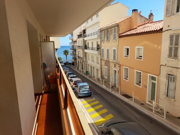 Un balcon donnant sur une rue bordée de voitures garées et d’immeubles.