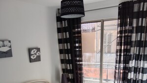 A bedroom with a bed, a window with curtains, a lamp, and a wall with two framed pictures. - Apartment very close to the sea (Toulon)