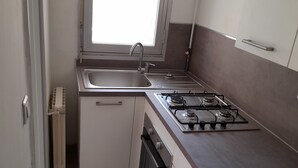 A compact kitchen with a window, a sink, a stove, and cabinets. - Apartment very close to the sea (Toulon)
