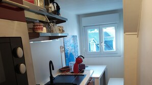 A compact kitchen with a stove, sink, and a window providing a view of the outside. - Apartment (Crozon)