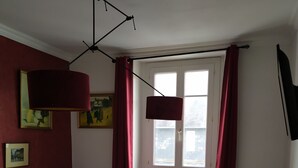 A hotel room with a bed, two armchairs, a small round table, a desk with a lamp, a window with curtains, and a TV mounted on the wall. - Apartment (Crozon)