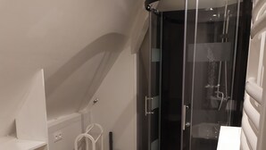 A modern bathroom with a glass shower enclosure, a white sink, and a patterned floor. - Apartment (Crozon)