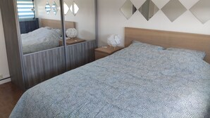 Een slaapkamer met een bed, nachtkastje, spiegel en een wandlamp.