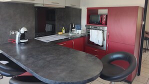 Een moderne keuken met een centraal eiland, rode kastjes, een magnetron en een koffieapparaat.