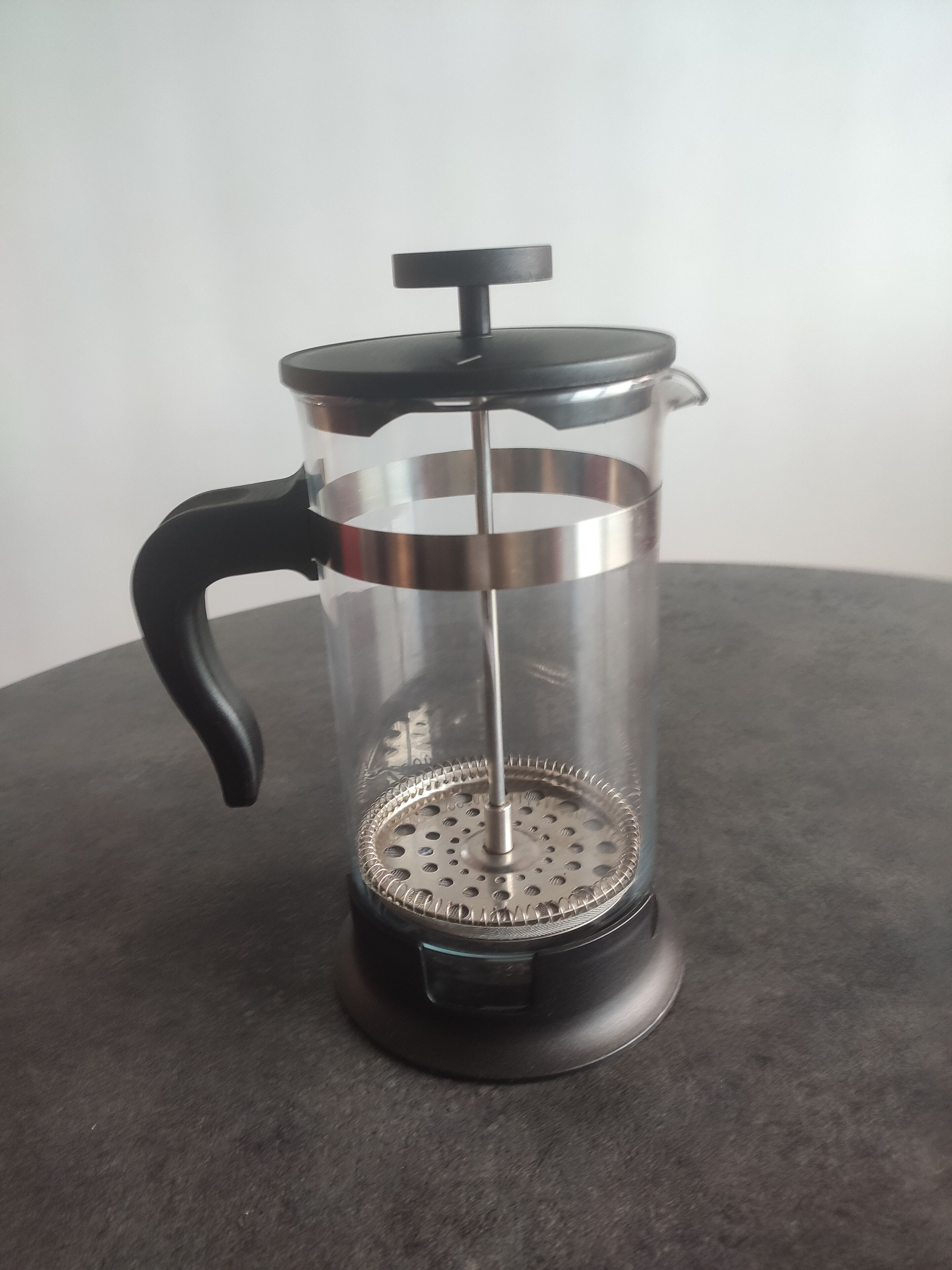 A French press coffee maker with a black handle and lid, placed on a dark surface.