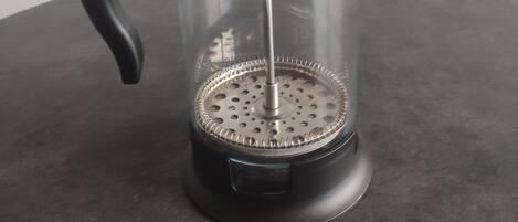 A French press coffee maker with a black handle and lid, placed on a dark surface.