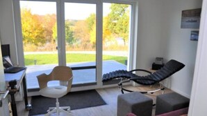 A room with a desk, a reclining chair, a small sofa, and a window with a view of trees.
