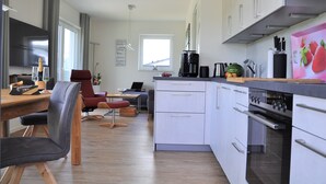 A modern kitchen with white cabinets, a built-in oven, and a dining area with a red chair and a wooden table.