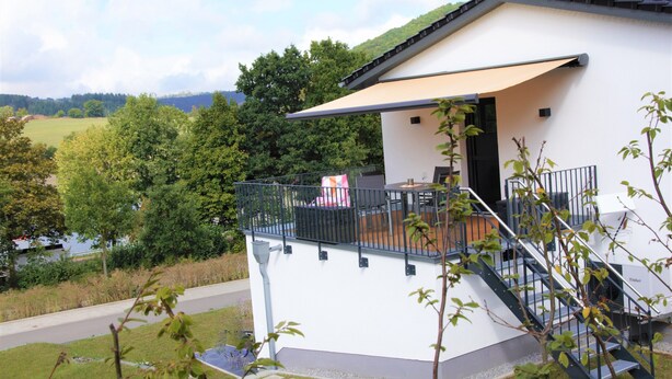 A modern building with a balcony, a staircase, and a view of a river and forest.