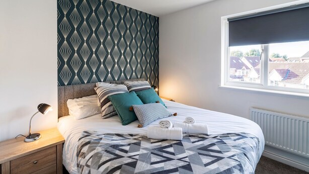 Un letto rifatto con cura, con una coperta a motivi geometrici, una lampada da comodino e numerosi cuscini.