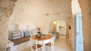 A rustic stone interior with a round wooden table, white chairs, and a bench with striped cushions. - TD Lamiamola Stylish Trulli Lamie With Pool (Ostuni)
