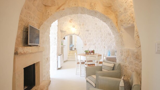 A cozy living area with a stone archway, a fireplace, and a dining table set for four. - TD Lamiamola Stylish Trulli Lamie With Pool (Ostuni)