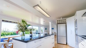 Una cocina moderna con una isla central, armarios blancos y un ventanal con vistas a un jardín.