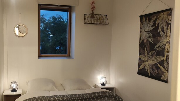 Quarto com cama, duas mesas de cabeceira com luminárias, uma janela e um espelho fixado na parede.