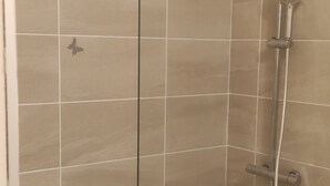 Área de chuveiro com porta de vidro, paredes revestidas com azulejos e uma pia branca à direita.