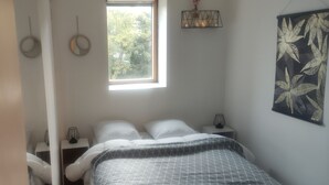 Quarto com cama, duas mesas de cabeceira, uma janela e uma planta fixada na parede.