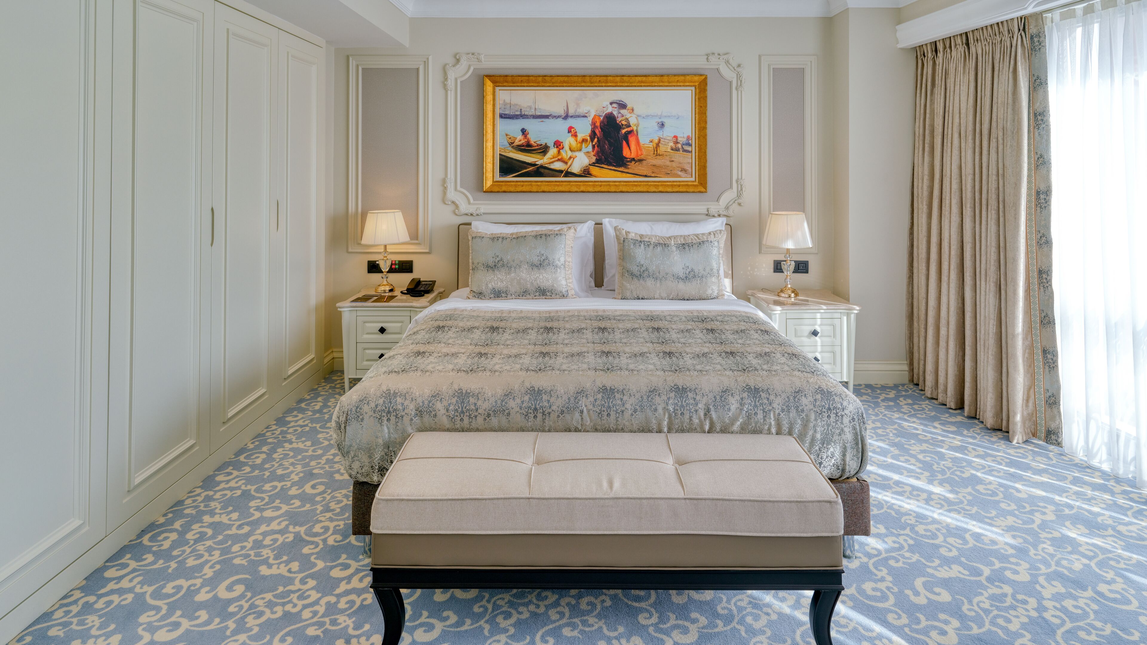 Une chambre spacieuse avec un grand lit, deux tables de chevet avec des lampes, un tableau au-dessus du lit et un tapis à motifs.