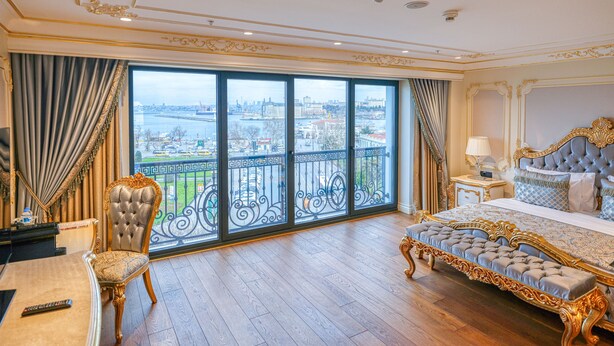 Um quarto luxuoso com uma cama grande, um chaise-longue e vista para o horizonte urbano através de janelas do chão ao teto.