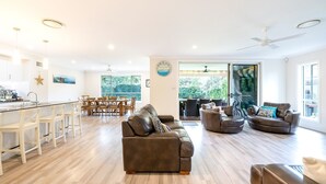 A spacious living area with a dining table, sofas, and a kitchen area with bar stools. - Big Wave At Shoal Bay, 8 Achilles St - large home with ducted air con, Wi-Fi and Linen (Nelson Bay)