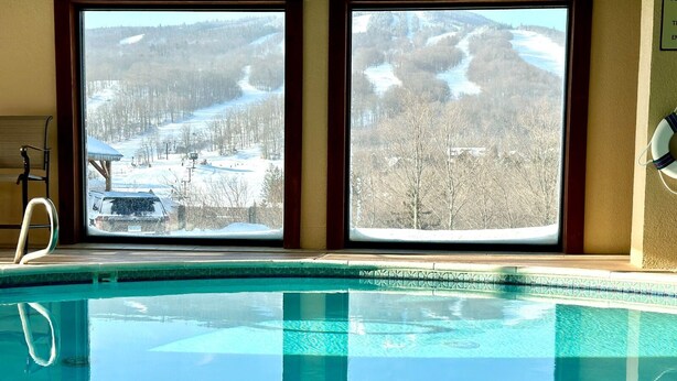Una piscina amb aigua clara i blava, dues finestres amb vistes a muntanyes nevades i un flotador a la dreta.