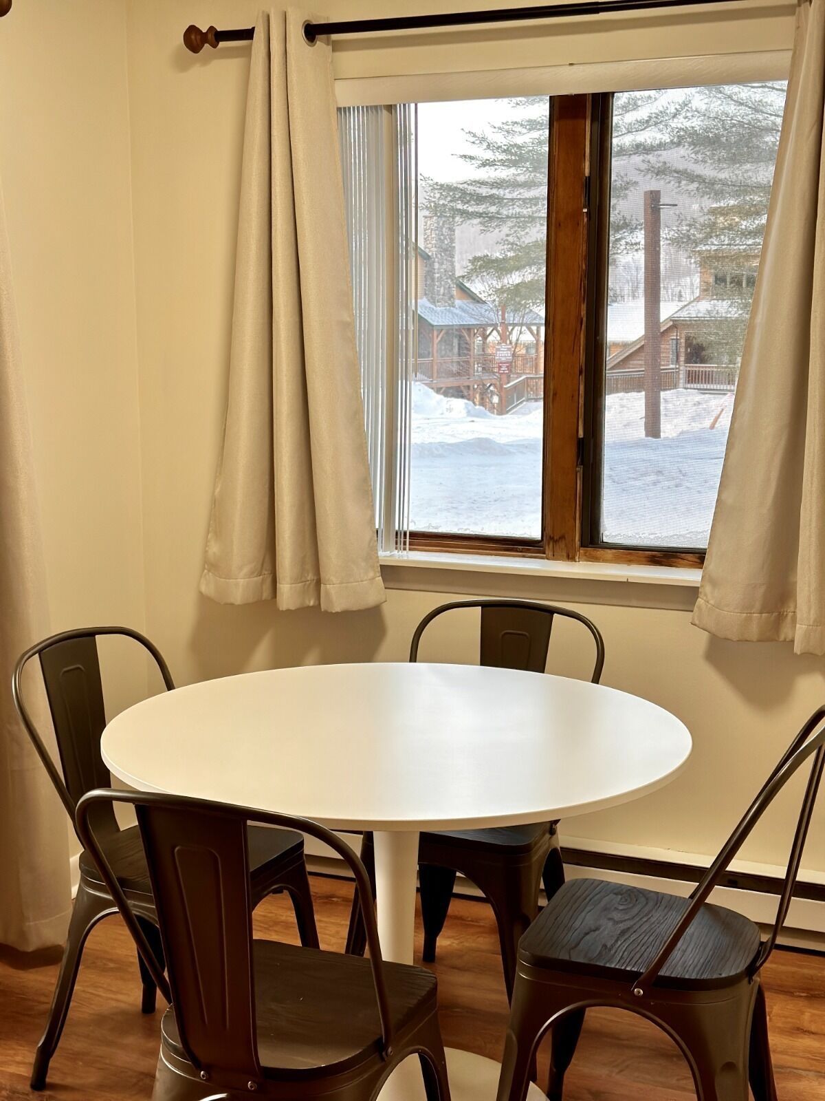 Une pièce avec une table ronde et quatre chaises, une fenêtre avec des rideaux et une vue sur un paysage enneigé.