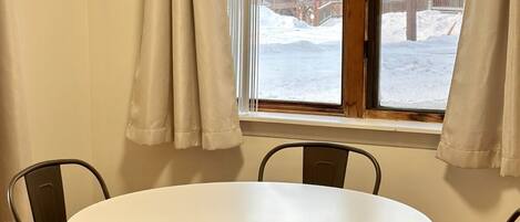 Une pièce avec une table ronde et quatre chaises, une fenêtre avec des rideaux et une vue sur un paysage enneigé.
