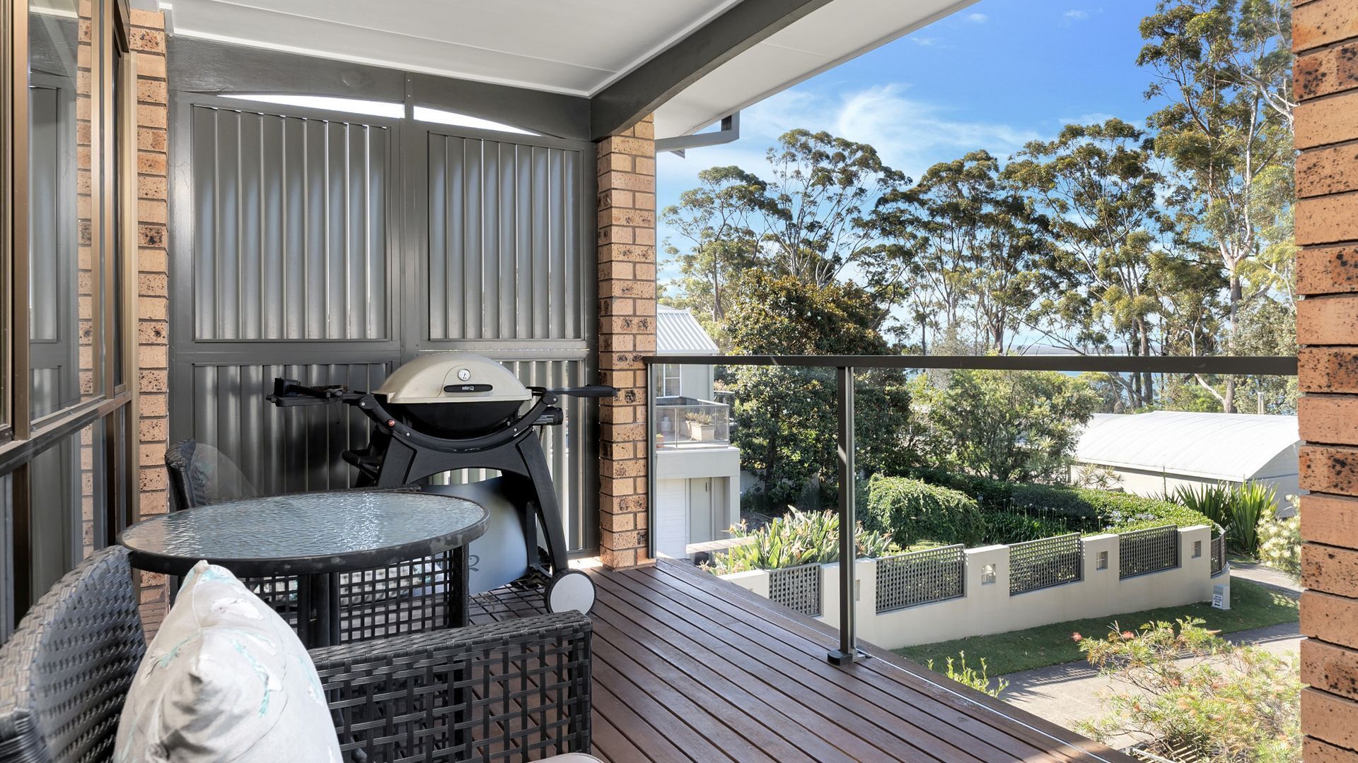 Ein Balkon mit Grill, rundem Tisch und Korbsessel.